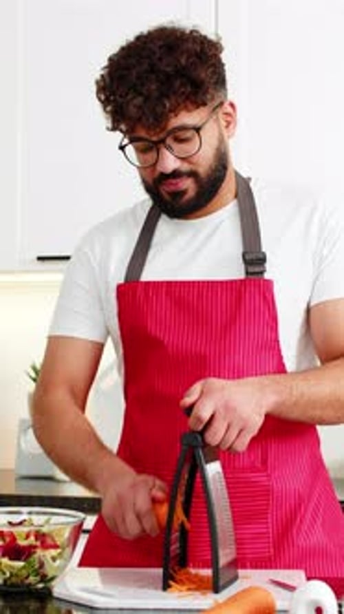 Man in Apron Grating Carrot in Bright Kitchen