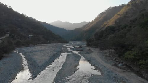 Aerial over river bed in tree covered valley with an excavator digging river rock for construction