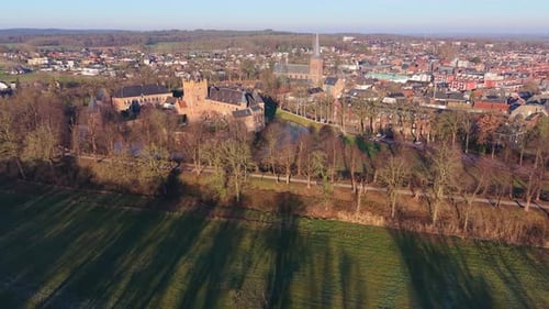 Aerial view of European town with red brick castle, moat, church spire, forest edge and grassy field