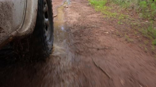Close-up of a car tire rolling through a puddle of water on a muddy road outdoors, splashing dirt