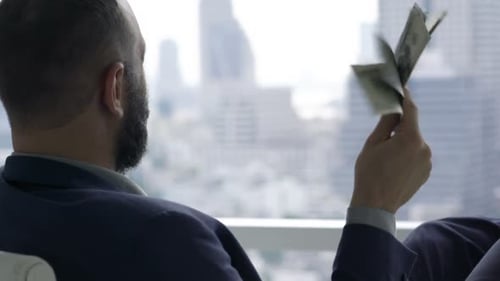 Successful, Happy Businessman Holding And Waving Money Sitting By Desk In Office