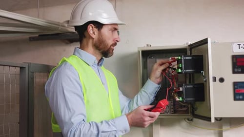 Electrician with Tester Checks Switchboard at Substation Examining Factory Lines