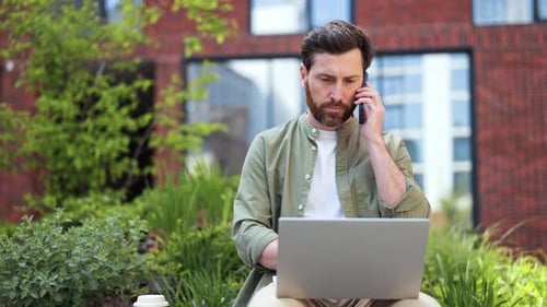 Man Working on Laptop Outdoors on Phone