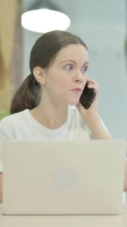 Angry Woman Talking on Phone at Laptop