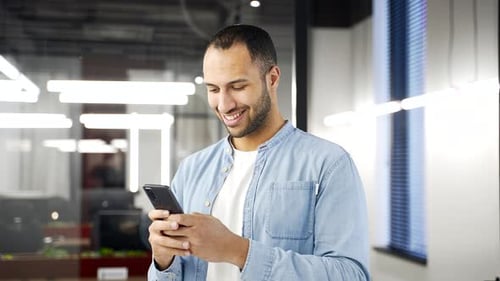 Smiling Man Using Smartphone in a Modern Office