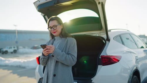 Woman Using Smartphone Near Car in Urban Setting