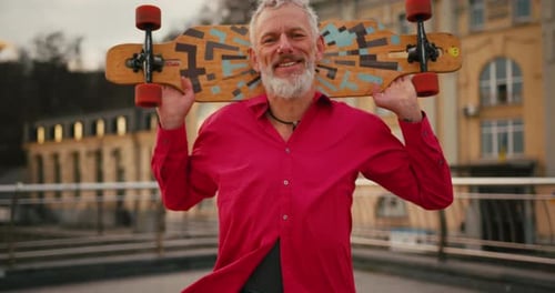Portrait of Active Cool Happy Older Senior Man Skater Wearing Red Shirt with Skateboard in City at