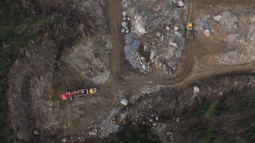 Excavator loads distant dump truck on rocky worksite