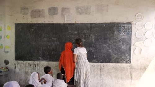 White caucasian teacher with muslim teacher writing on the blackboard numbers teaching black african