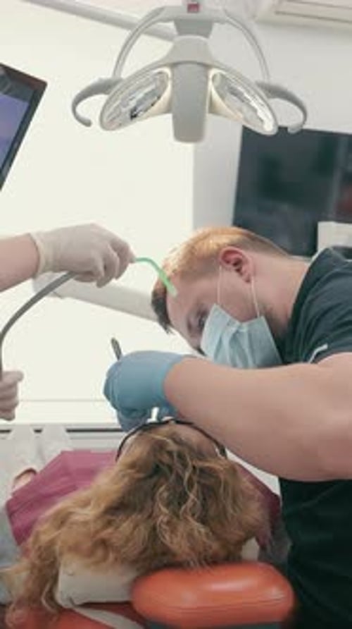 Dentist and His Assistant in Protective Masks Treat a Patient's Teeth in a Dental Clinic Healthcare