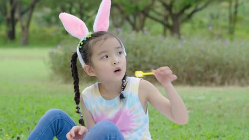Happy little asian girl kid blowing soap bubbles playing alone in the park