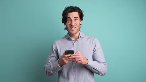 Surprised Man with Cellphone Celebrating Victory in Blue Studio
