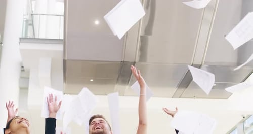A group of businesspeople throwing paperwork and high five in their workplace
