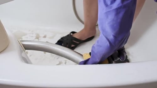 Person Cleaning Bathtub with Sponge and Gloves