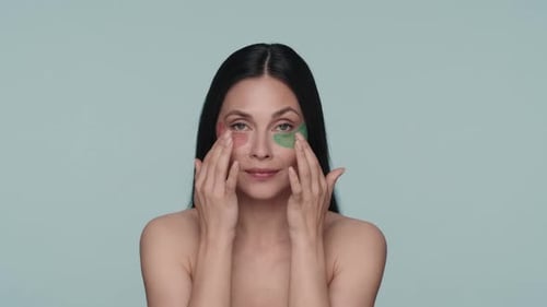 Portrait of a Seminude Woman with Various Hyaluronic Patches Under Her Eyes on a Blue Background