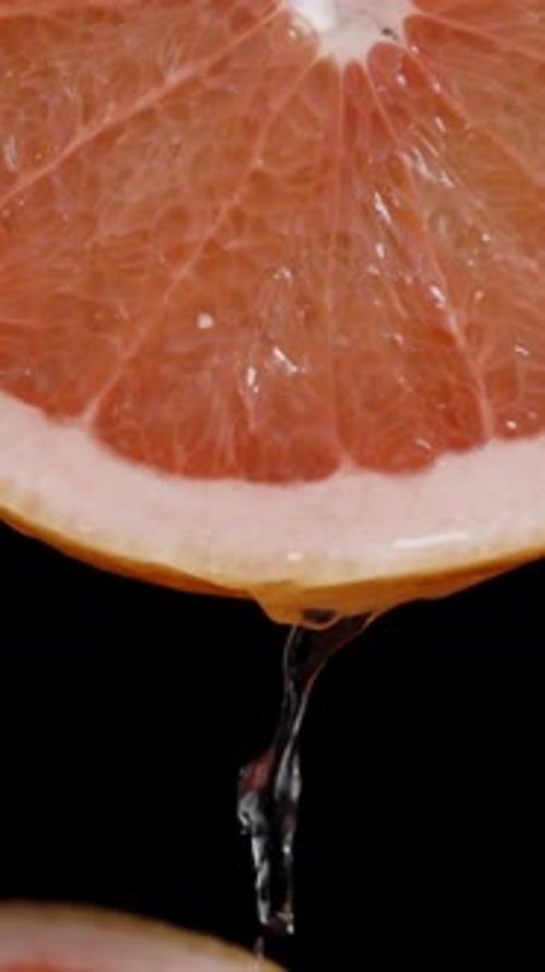 Vertical.From The Top, Juice Drips From A Grapefruit Slice Onto Other Slices, On A Black Background.