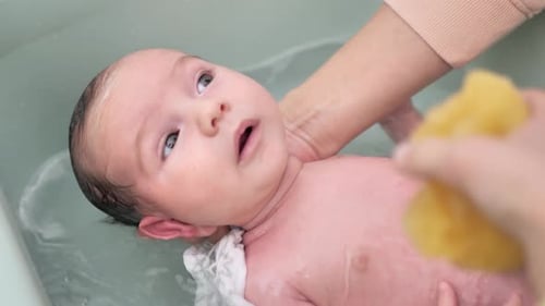 Nahaufnahme der Hand einer Mutter, die auf dem Rücken ihres Sohnes in warmem Wasser badet