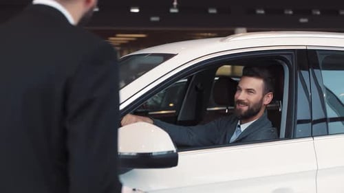 Happy Attractive Man Sitting at Wheel of Car in Prestigious Car Dealership Seller in Black Business