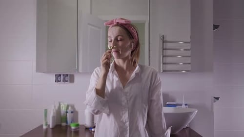 A Young Pretty Woman Wriggles and Smoothes the Skin of the Face with a Roller