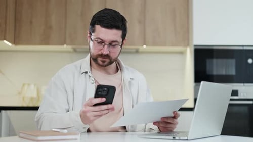 Competent Male Looking From Document to Tphone During Work Process at Home