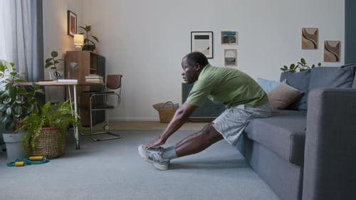 Elderly Black Man Doing Forward Bend and Tricep Press on Couch at Home