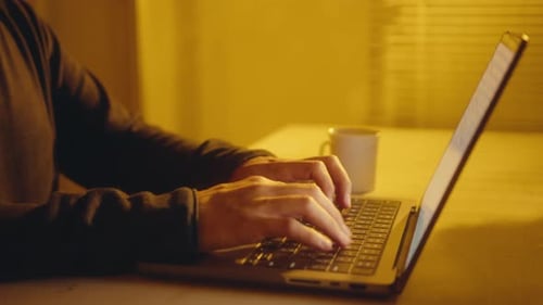 Männliche Hände tippen auf Laptop im Raum mit gelbem Licht
