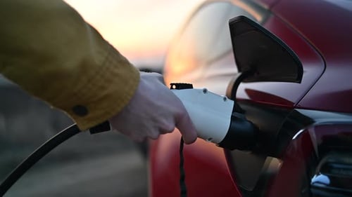 Mann lädt bei Sonnenuntergang ein rotes Elektroauto auf