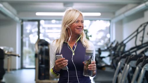 A Senior Woman With Smartphone In Gym Resting After Doing Exercise.