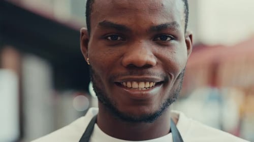 Retrato de cerca de un joven camarero afroamericano con una amplia sonrisa de pie al aire libre