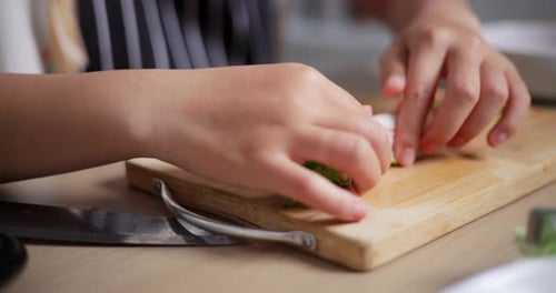 Beautiful young woman in striped apron making salad rolls, cooking at home