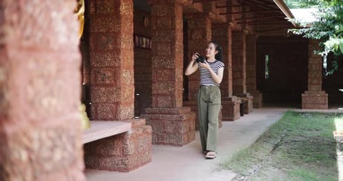 Young Asian woman walks around an ancient site and takes photos with her camera.