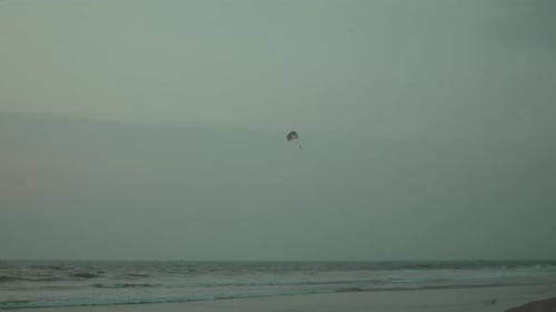 Aerial view of parasailing over calm beach and ocean with distant sunset horizon