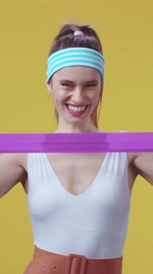 Smiling Woman Exercising with Resistance Band on Yellow Background