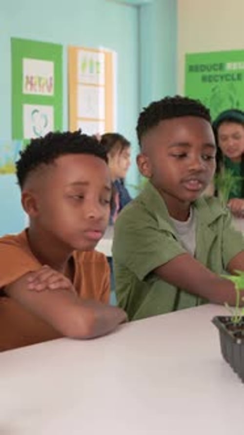 Vertical video: Reacting to demo, green-shirt boy adjusting wind turbines in class, with tablet