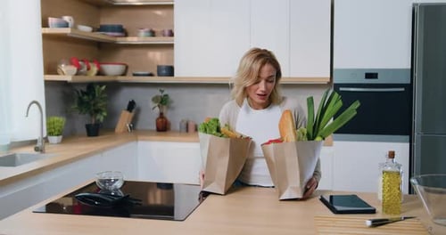 Consumidora femenina desempaca sus alimentos de una bolsa de papel ecológica de pie en una cocina moderna.