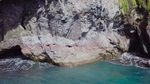 Drone shot of seaside cliff caves with waves lapping at rocks. Slow panning shot.