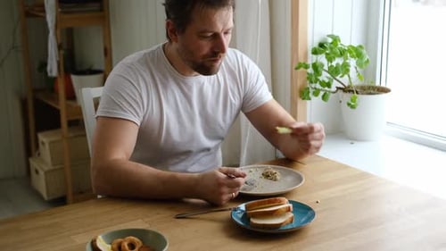 Handsome Bearded Man is Eating Green Fresh Vegan Salad in the Kitchen at Home Male Sitting at Table