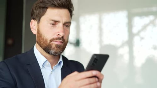 Businessman in formal suit is using smartphone at workplace in business office. Worker reads