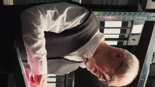 Senior Man Works at Dimly Lit Desk