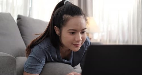 Joven asiática deportiva viendo un Vídeo tutorial de acondicionamiento físico en línea en el portátil mientras se acuesta en el sofá