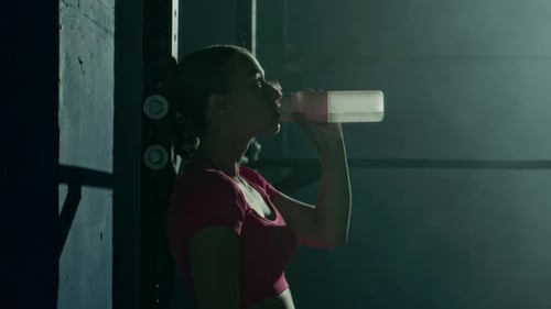Young Woman Drinking Water and Wiping off Swear from Forehead after Gym Workout