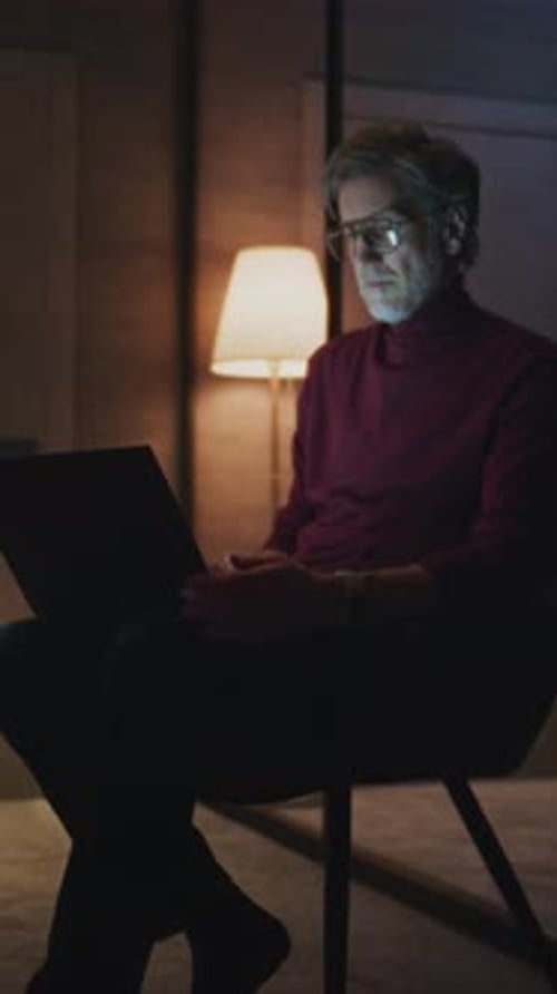 Mature Traveler Works on Laptop in Softly Lit Modern Hotel Room at Night