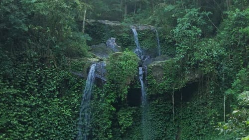 Drone flying forward to natural waterfall cascade in the heart of a dense jungle
