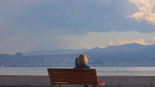Blonde Woman Sitting On The Bench On The City Beach Watching The Sea View