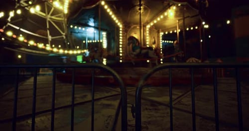 Vintage Illuminated Carousel Rotating at Night Behind a Fence