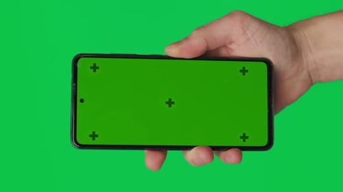 Male Hand Holding a Smartphone with Vertical Green Chroma Key Screen Isolated on Green Background