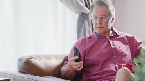 Senior caucasian man sitting on sofa and using smartphone, slow motion
