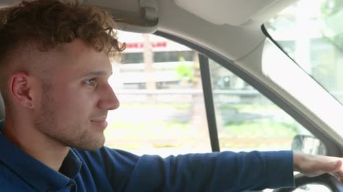 Side View of Caucasian Handsome Joyful Male Driver Sitting in Car with His Hands on Steering Wheel