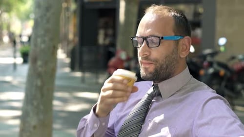 Young Businessman Relaxing and Drinking Coffee Sitting on Bench in City 30s