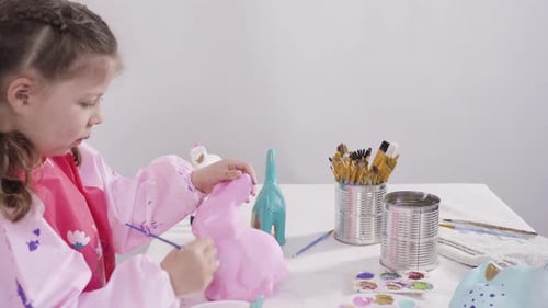 Little Girl Painting Paper Mache Figurines with Acrylic Paint for Her Homeschooling Art Project